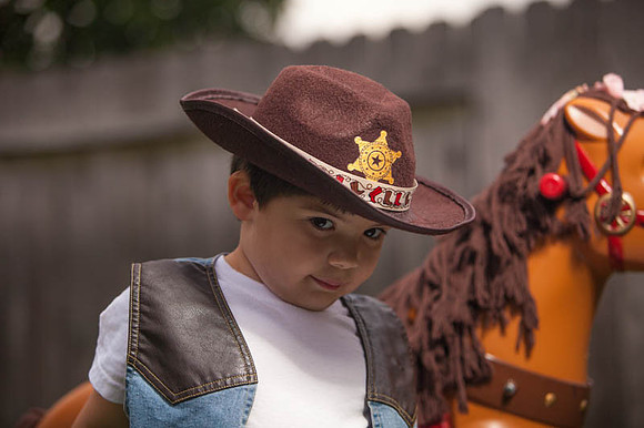 Boy Dressed as a Cowboy Standing Next to Toy Horse