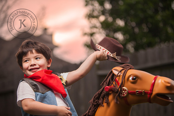 Boy Dressed as Cowboy Riding a Toy Horse with Hat in Hand