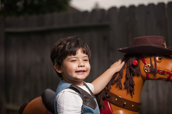Boy Dressed as a Cowboy Putting Hat on Toy Horse